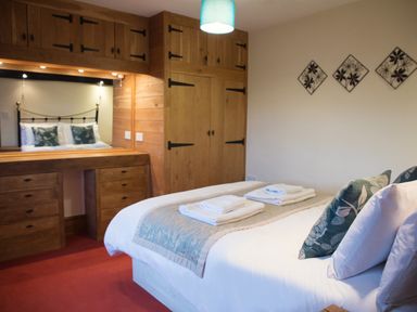 A bedroom with a double bed with pillows and towels on it and wooden wardrobes at Yew Tree Cottage in Little Malvern near Malvern