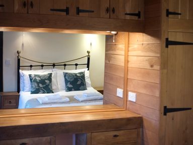 A bedroom with a double bed with white linens and patterned pillows reflected in a mirror above a wooden dresser at Yew Tree Cottage in Little Malvern near Malvern