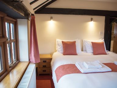 A bedroom with a double bed white towels bedside table and window at Yew Tree Cottage in Little Malvern near Malvern