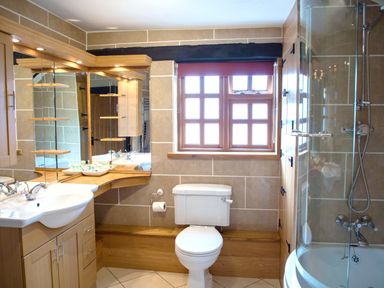 A bathroom with a toilet sink wooden cabinets and a glass enclosed shower at Yew Tree Cottage in Little Malvern near Malvern