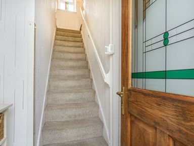 A carpeted staircase with white walls and a wooden door with patterned glass at Hillside Cottage in Peasedown St John near Bath