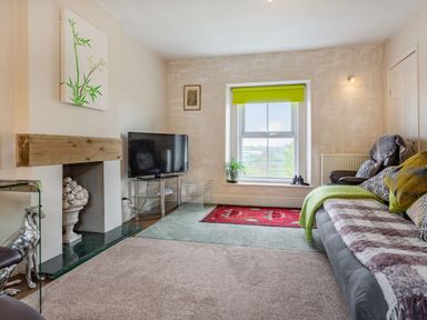 A living room with a television a sofa and a window with a green blind at Hillside Cottage in Peasedown St John near Bath
