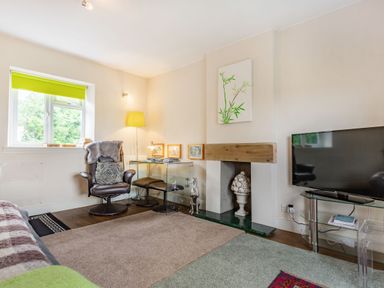 A living room with a leather chair and glass side table near a fireplace and a television on a glass stand at Hillside Cottage in Peasedown St John near Bath
