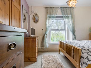 A bedroom with wooden furniture a bed with zebra patterned bedding a window with sheer curtains and a small television on a dresser at Hillside Cottage in Peasedown St John near Bath