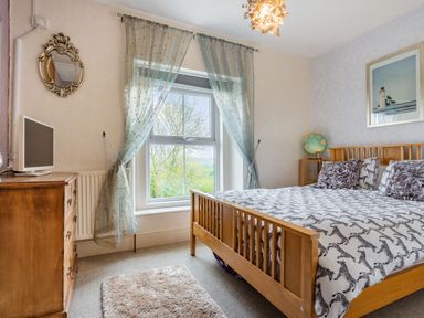 A bedroom with a wooden bed a dresser a small television and a window with curtains at Hillside Cottage in Peasedown St John near Bath