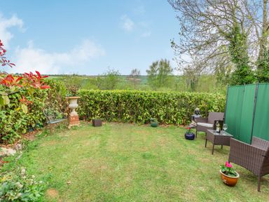 A garden with chairs a table potted plants and a statue at Hillside Cottage in Peasedown St John near Bath