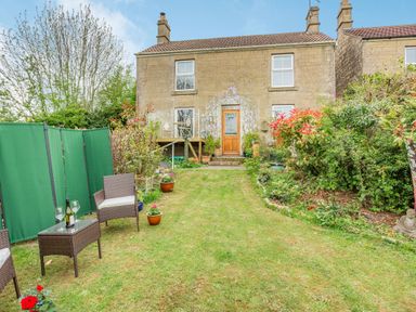 A garden with chairs a table and plants in front of a stone house at Hillside Cottage Peasedown St John near Bath