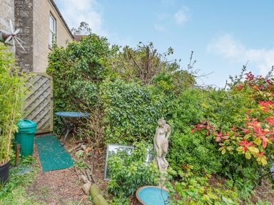 A garden area with a statue a birdbath a small table and chair and a wooden gate at Hillside Cottage in Peasedown St John near Bath