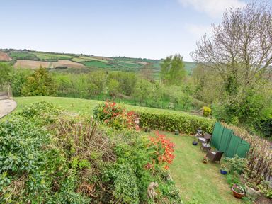 A garden with chairs a table potted plants and statues with countryside fields in the background at Hillside Cottage in Peasedown St John near Bath