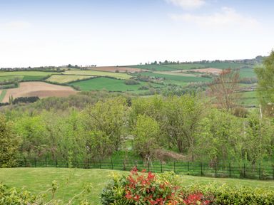 A view of rolling fields and trees with a lawn and bushes in the foreground at Hillside Cottage in Peasedown St John near Bath
