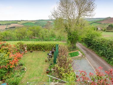 A garden with chairs and plants next to a gravel driveway and countryside fields beyond at Hillside Cottage in Peasedown St John near Bath
