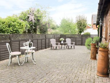 An outdoor patio area with a small white table and two chairs and two plastic chairs with a small side table and potted plants along a stone wall at High Park Barn in Uffculme Blackdown Hills