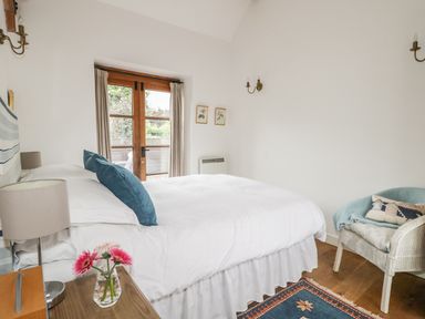 A bedroom with a bed pillows a chair flowers on a table and wooden door at High Park Barn in Uffculme Blackdown Hills