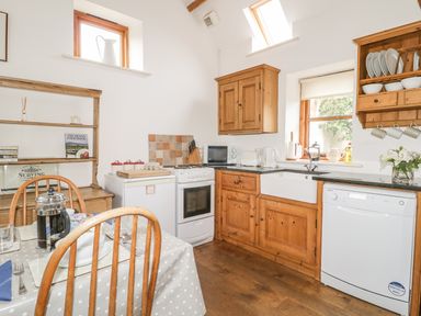 A kitchen with wooden cabinets a dining table with chairs and kitchen appliances at High Park Barn in Uffculme Blackdown Hills