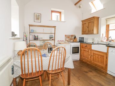 A kitchen with wooden cabinets a dining table with four chairs and kitchen appliances at High Park Barn in Uffculme Blackdown Hills