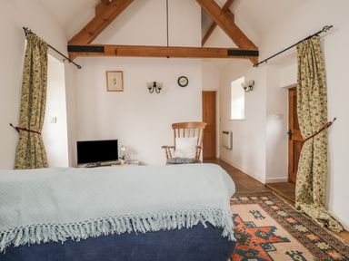A living room with wooden beams a rocking chair and a television at High Park Barn in Uffculme Blackdown Hills