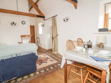A room with a dining table set for two wooden chairs a blue sofa a wooden rocking chair and exposed wooden beams at High Park Barn in Uffculme Blackdown Hills