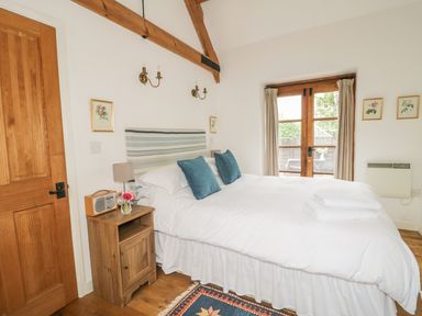 A bedroom with a double bed two blue pillows wooden side table with radio and flowers wooden door and glass doors to outside at High Park Barn in Uffculme Blackdown Hills