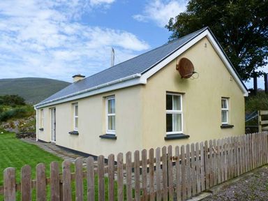 A small beige house with a grey roof and wooden fence in front at The Bay in Caherdaniel County Kerry