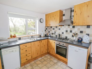 A kitchen with wooden cabinets, a gas stove, oven, dishwasher, fridge, sink, and a window at Mary Kates Cottage in Narin County Donegal