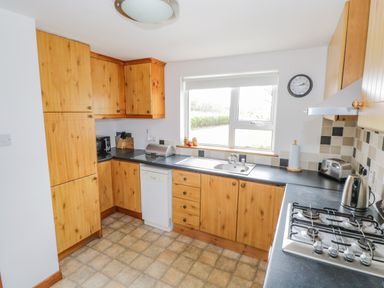 A kitchen with wooden cabinets a gas stove a sink and a window at Mary Kates Cottage in Narin County Donegal