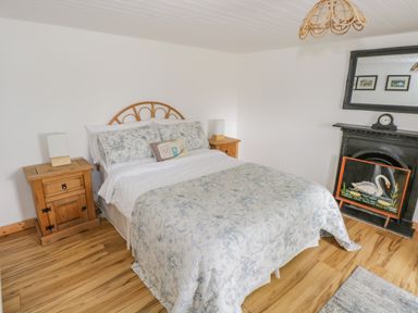 A bedroom with a bed flanked by wooden nightstands and a fireplace with a swan painting at Mary Kates Cottage in Narin County Donegal