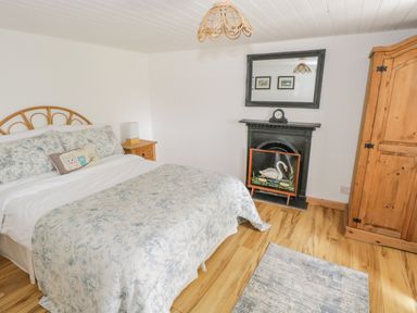 A bedroom with a bed a wooden wardrobe a nightstand a fireplace with a swan painting and a mirror above at Mary Kates Cottage in Narin County Donegal