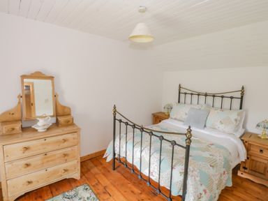 A bedroom with a metal bed frame wooden dressers and a wooden floor at Mary Kates Cottage in Narin County Donegal
