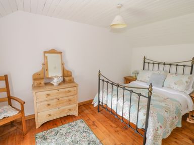 A bedroom with a metal frame bed wooden dresser with mirror and wooden chair at Mary Kates Cottage in Narin County Donegal