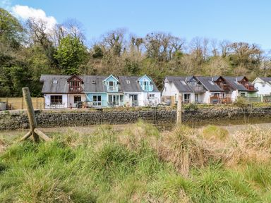 A row of houses with balconies behind a stone wall and grassy area at Waterside Cottage in Little Petherick Creek near Padstow