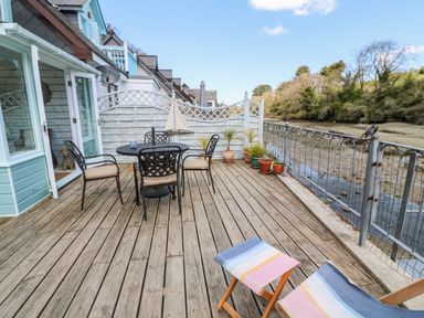 A wooden deck with outdoor table and chairs and potted plants overlooking a river at Waterside Cottage in Little Petherick Creek near Padstow