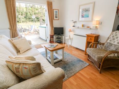 A living room with a sofa pillows coffee table armchair television and open doors to a deck at Waterside Cottage in Little Petherick Creek near Padstow