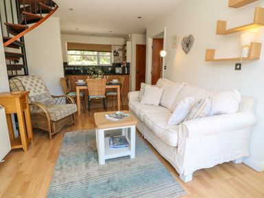A living room with a white sofa a small table and an armchair next to a dining table with chairs and a kitchen in the background at Waterside Cottage in Little Petherick Creek near Padstow