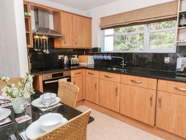 A kitchen with wooden cabinets black countertops a stainless steel oven and dining table with dishes at Waterside Cottage in Little Petherick Creek near Padstow