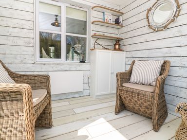 A sunroom with wicker chairs striped cushions white cabinet and shelves with nautical decorations at Waterside Cottage in Little Petherick Creek near Padstow