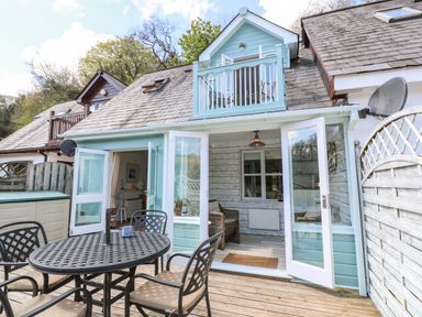 An outdoor patio area with a round table and four chairs outside a house with blue and white exterior and glass doors at Waterside Cottage in Little Petherick Creek near Padstow
