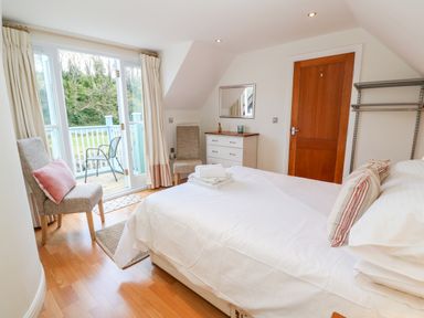 A bedroom with a bed towels two chairs a chest of drawers and a balcony at Waterside Cottage in Little Petherick Creek near Padstow