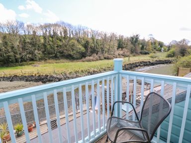 A balcony with a metal chair overlooking a river and trees at Waterside Cottage in Little Petherick Creek near Padstow