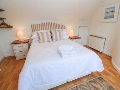 A bedroom with a double bed with striped cushions and headboard bedside tables with lamps wooden floor and a framed painting at Waterside Cottage in Little Petherick Creek near Padstow