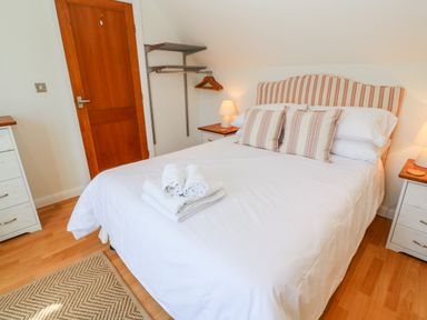 A bedroom with a double bed white bedding striped pillows bedside tables with lamps a wooden door and shelves at Waterside Cottage in Little Petherick Creek near Padstow
