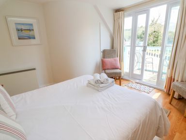 A bedroom with a made bed with folded towels on it two chairs one with a pink cushion and glass doors leading to a balcony at Waterside Cottage in Little Petherick Creek near Padstow