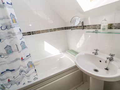 A bathroom with a bathtub a shower curtain a sink and a wall-mounted mirror at Waterside Cottage in Little Petherick Creek near Padstow
