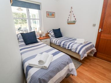 A bedroom with two single beds striped bedding a window and a wooden door at Waterside Cottage in Little Petherick Creek near Padstow
