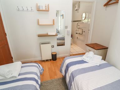 A bedroom with two single beds with striped bedcovers and towels on them a wooden nightstand a wall mirror and shelves at Waterside Cottage Little Petherick Creek near Padstow