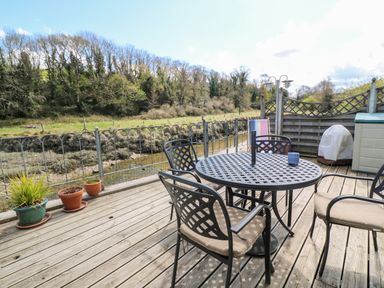 A patio with a round metal table and four chairs beside a river and trees at Waterside Cottage in Little Petherick Creek near Padstow