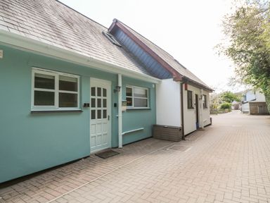 Exterior view of a row of houses with paved driveway and trees on the right at Waterside Cottage in Little Petherick Creek near Padstow