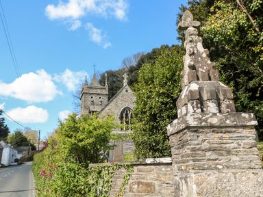 A stone church with a tower and cross near a road lined with bushes and hedges