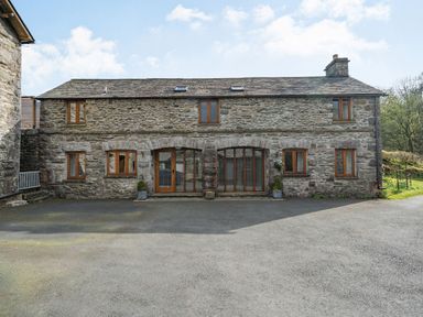 Stone cottage with multiple wooden windows and two large wooden doors with glass at Moresdale Bank Cottage in Lambrigg near Sedbergh and Kendal