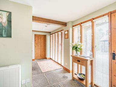 A hallway with stone floor wooden door console table with flowers and a bowl and windows with blinds at Moresdale Bank Cottage Lambrigg near Sedbergh and Kendal