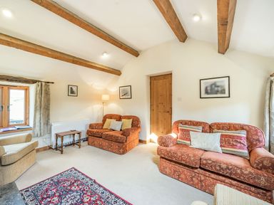 A living room with wooden ceiling beams two patterned sofas an armchair a small wooden table a floor lamp and framed pictures at Moresdale Bank Cottage Lambrigg near Sedbergh and Kendal